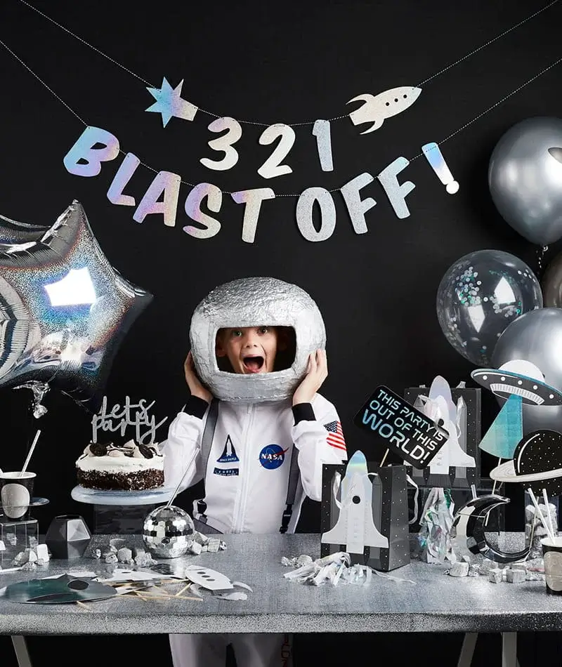 Space-themed birthday party setup with astronaut decorations, rocket accents, silver balloons, a birthday cake, and a Blast Off party banner. Space-themed birthday party setup with astronaut decorations, rocket accents, silver balloons, a birthday cake, and a Blast Off party banner.